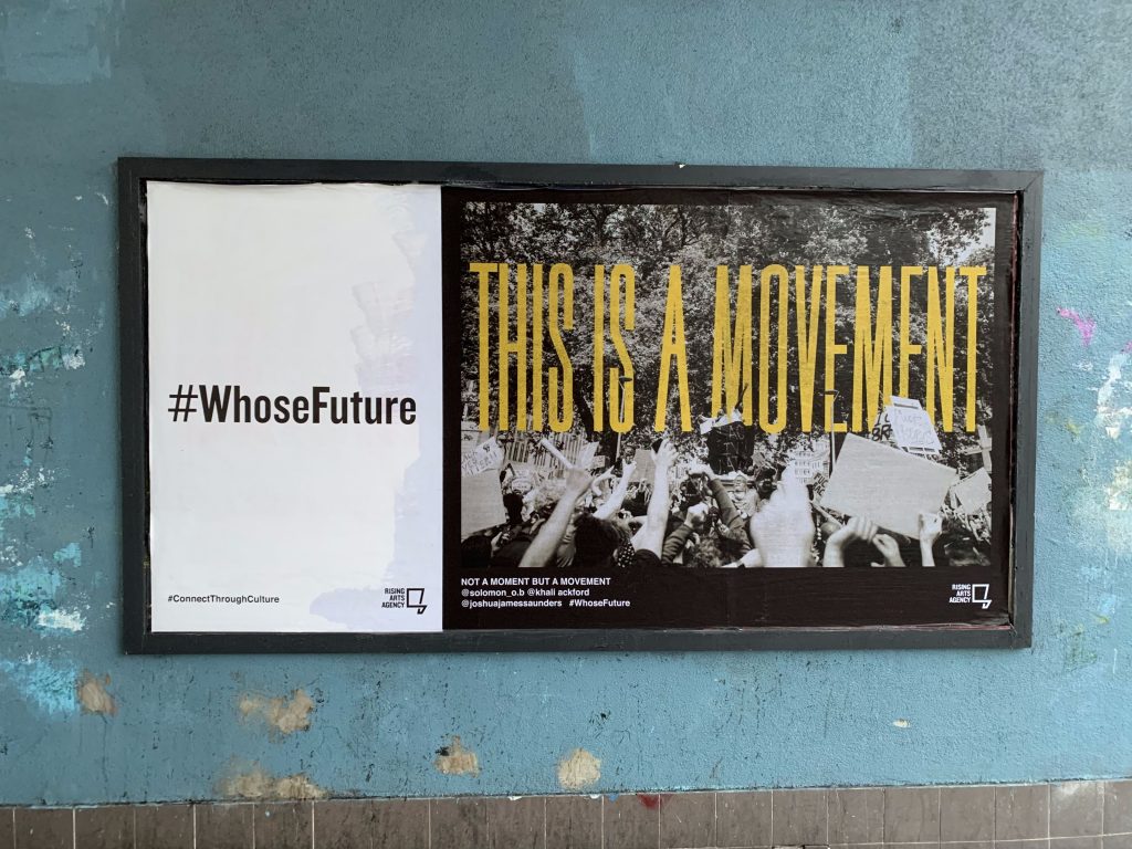 A #WhoseFuture campaign billboard which displays an edited black and white photograph of the empty Colston plinth at the Bristol BLM protest in June 2020, with the words 'This is a movement' overlayed in yellow