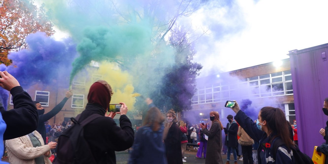Students on the University of Manchester campus in Owen's Park holding up cans of multi-coloured smoke