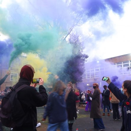 Students on the University of Manchester campus in Owen's Park holding up cans of multi-coloured smoke
